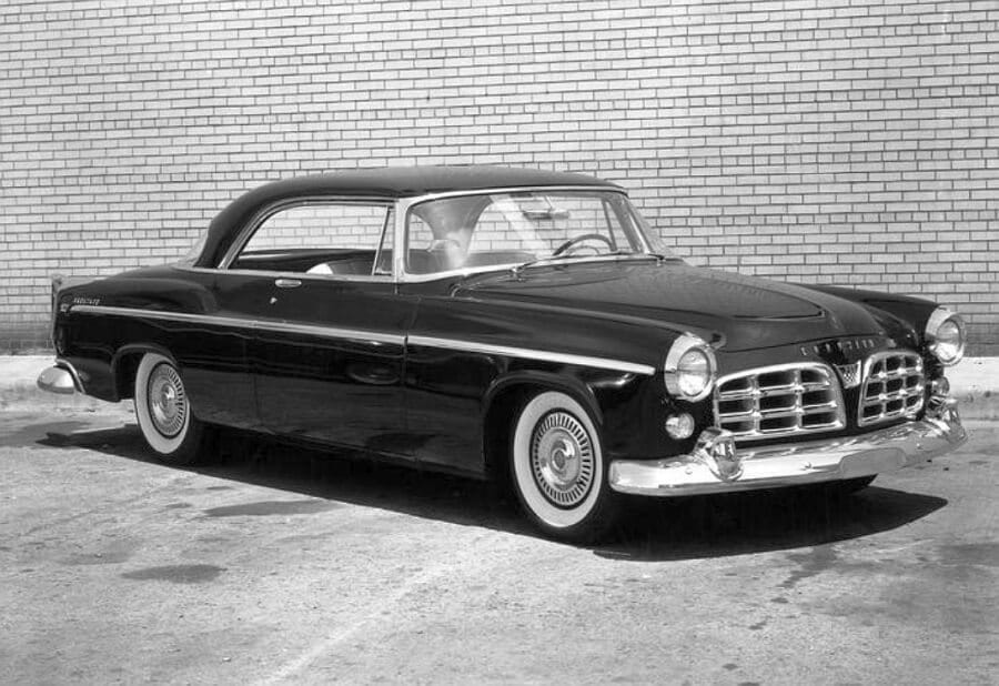 Zabytkowe coupe marki Chrysler na tle ceglanego muru, z białymi oponami i chromowanymi elementami.