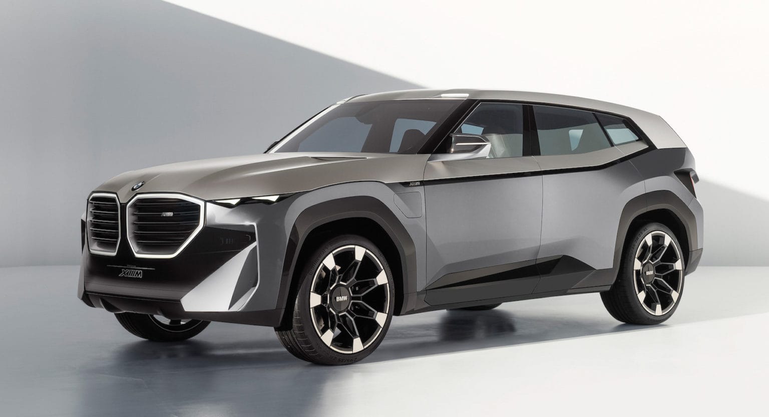 Srebrny prototyp SUV-a BMW XM stoi w jasnym, minimalistycznym studiu, w którym pojawiają się geometryczne cienie.